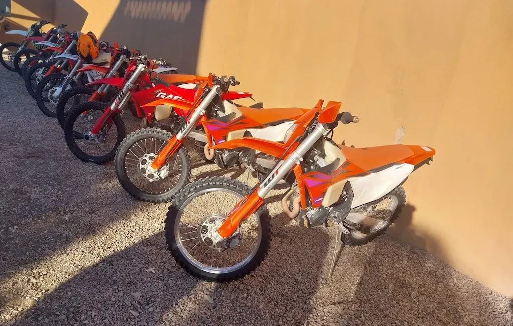 Flota de motos en el desierto Fila de motos de enduro aparcadas en línea sobre la arena del desierto al atardecer.