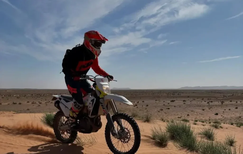 Piloto de enduro atravesando una zona de dunas suaves en el desierto del Sahara.